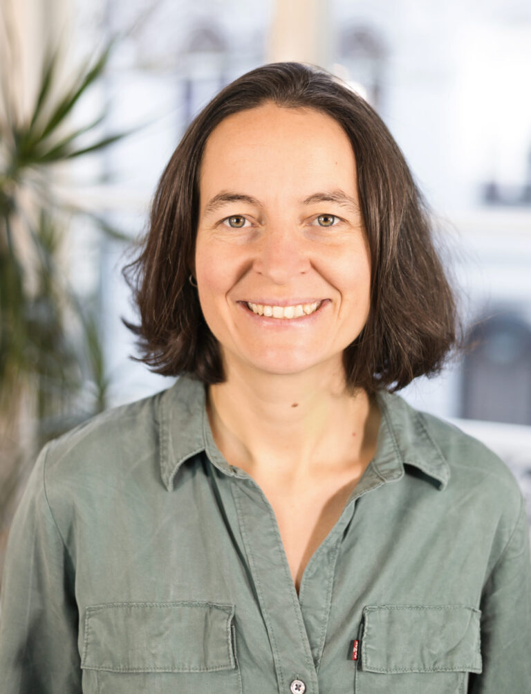 Eine Frau mit dunklen Haaren lächelt in die Kamera. Sie trägt eine hellgrüne Bluse.