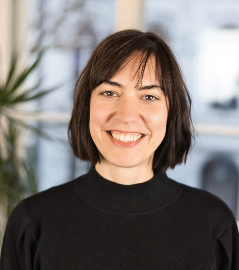 Eine Frau mit schwarzen Haaren und Pony lächelt in die Kamera. Sie trägt einen schwarzen Pullover.