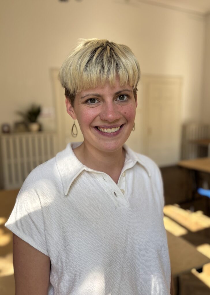 Eine Frau mit kurzen blonden Haaren und weißem Hemd lächelt in die Kamera.