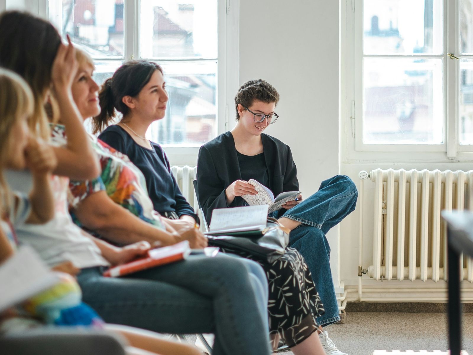 Vier Frauen sitzen in einer Reihe und höhren jemandem zu, eine Frau hat ein Notizbuch auf dem Schoß.