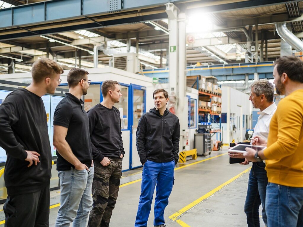 Menschen stehen in einer Industriehalle und unterhalten sich