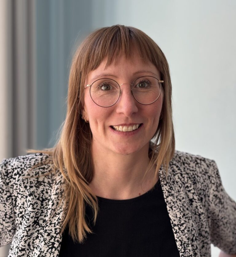 Eine Frau mit roten Haaren und Brille lächelt in die Kamera.